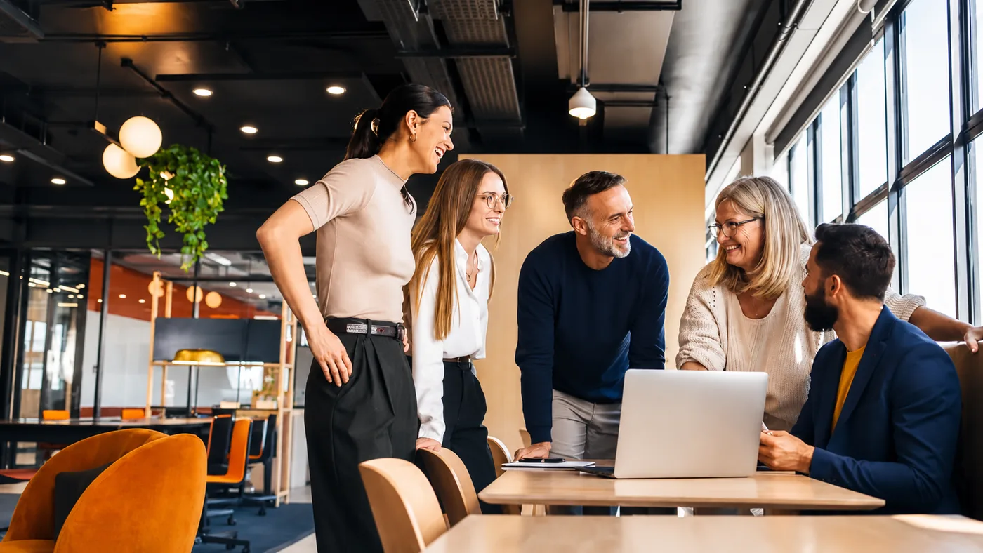 F&uuml;nf Personen besprechen ein Projekt am Laptop in einem hellen B&uuml;ro