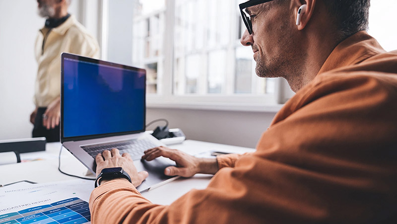 Mann mit Brille sitzt vor einem Laptop und schreibt über die Tastatur