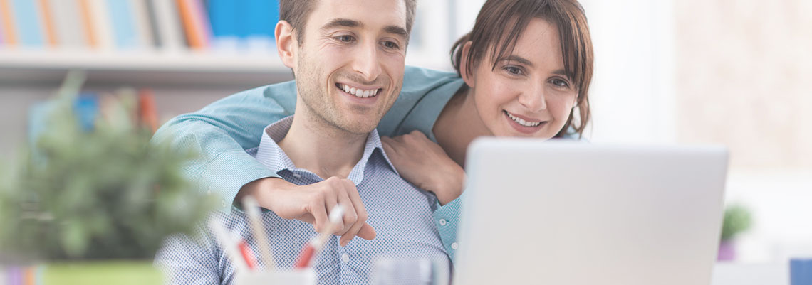 Mann und Frau, die sich lächelnd eine Website auf einem Laptop anschauen